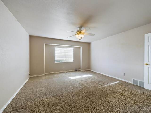 carpeted spare room featuring a ceiling fan, visible vents, and baseboards