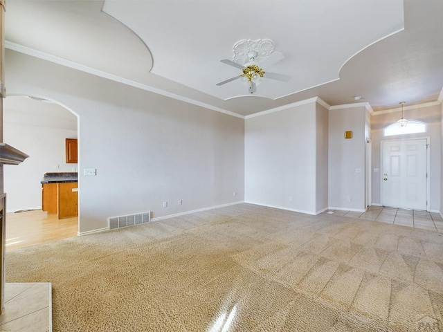 unfurnished living room with visible vents, arched walkways, light colored carpet, ceiling fan, and ornamental molding