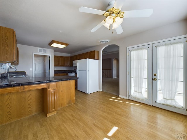 kitchen with white appliances, arched walkways, visible vents, brown cabinets, and a sink