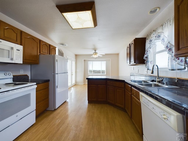 kitchen featuring light wood-style floors, dark countertops, white appliances, and a sink