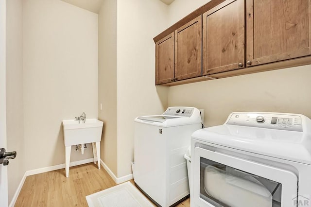 laundry room with washer and clothes dryer, cabinet space, light wood-type flooring, and baseboards