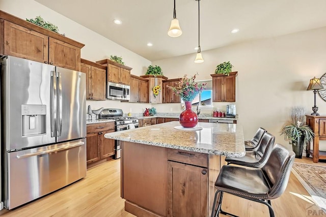 kitchen with a center island, decorative light fixtures, light stone counters, appliances with stainless steel finishes, and light wood-style floors