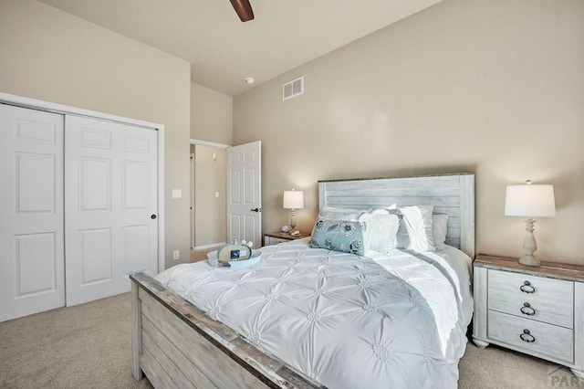 bedroom with visible vents, a ceiling fan, a closet, lofted ceiling, and light colored carpet