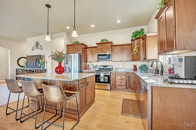 kitchen featuring a breakfast bar, a sink, light wood-style floors, appliances with stainless steel finishes, and a center island