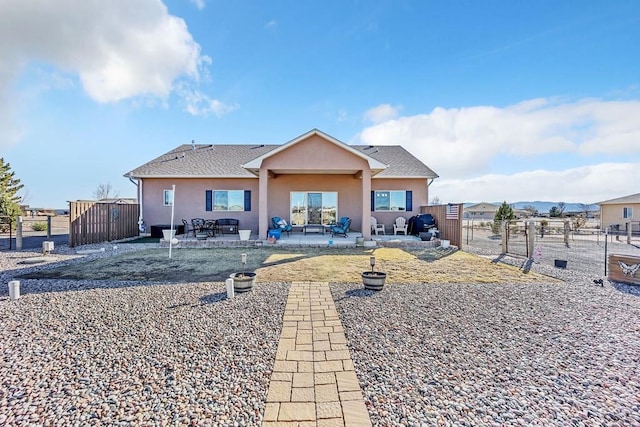 rear view of property featuring stucco siding, fence, a shingled roof, and a patio area