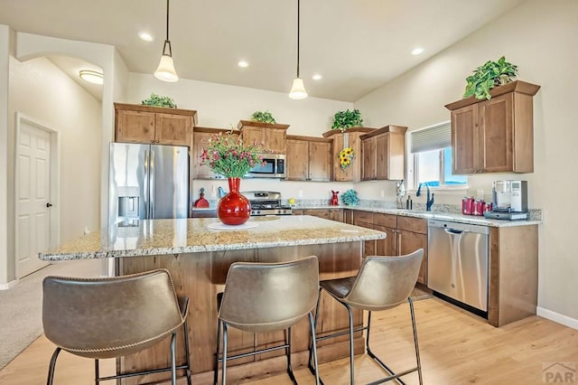 kitchen featuring light wood finished floors, a kitchen island, light stone counters, stainless steel appliances, and a sink