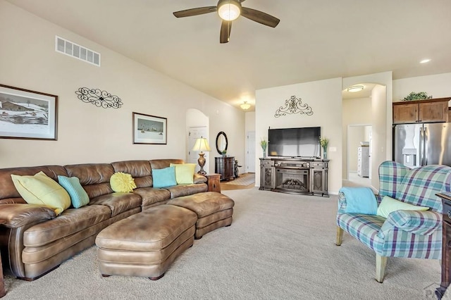 carpeted living room featuring a ceiling fan, vaulted ceiling, arched walkways, and visible vents