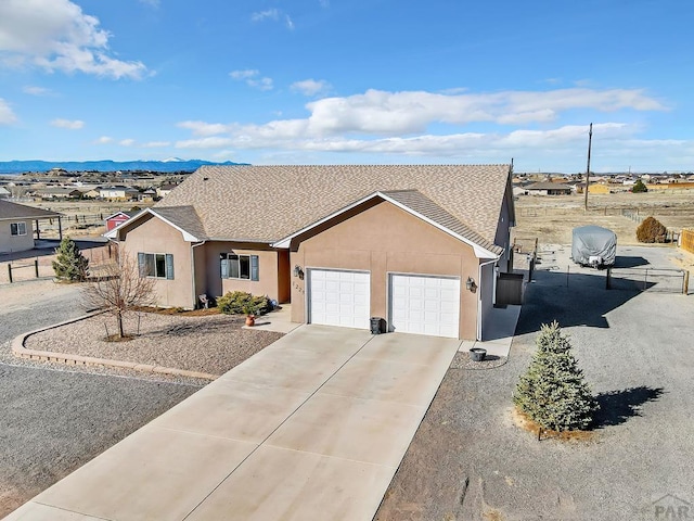 ranch-style home with roof with shingles, driveway, an attached garage, stucco siding, and a mountain view