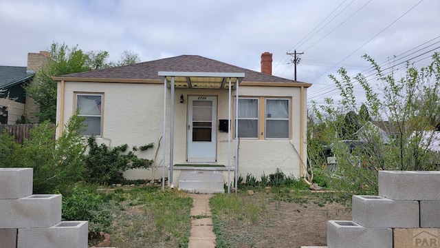 bungalow-style house with a chimney, stucco siding, and roof with shingles