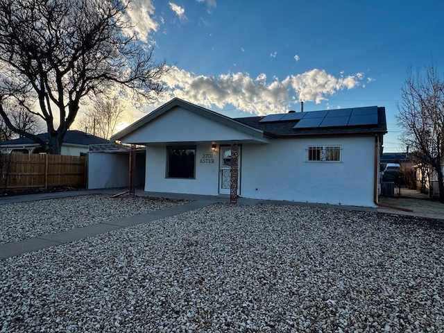 view of front of home featuring a shingled roof, fence, solar panels, and stucco siding