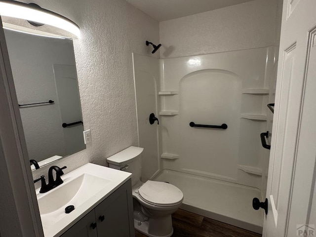 bathroom with a textured wall, toilet, wood finished floors, vanity, and a shower