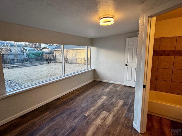 empty room featuring a textured ceiling, baseboards, dark wood-type flooring, and a textured wall