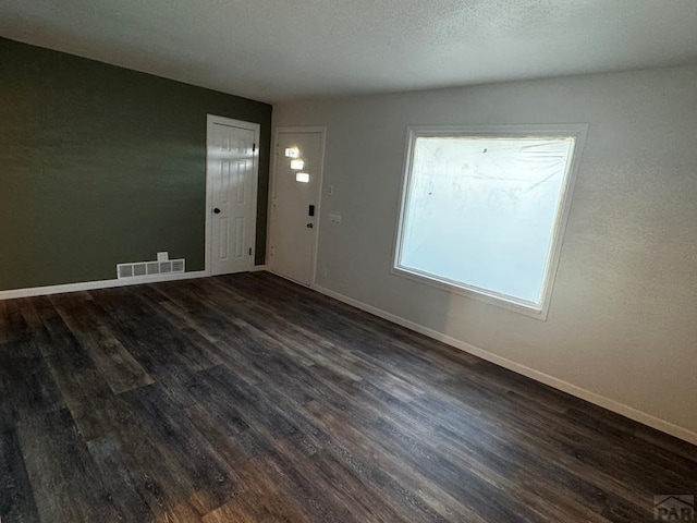 spare room with a textured ceiling, dark wood-type flooring, visible vents, and baseboards