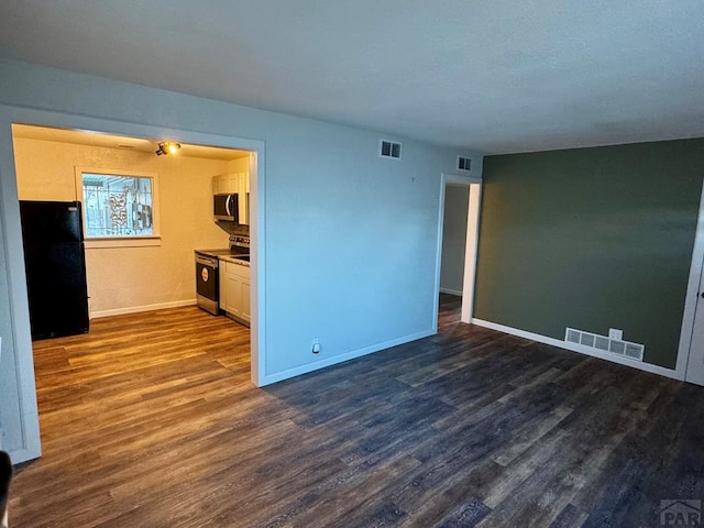 spare room with dark wood-type flooring, visible vents, and baseboards