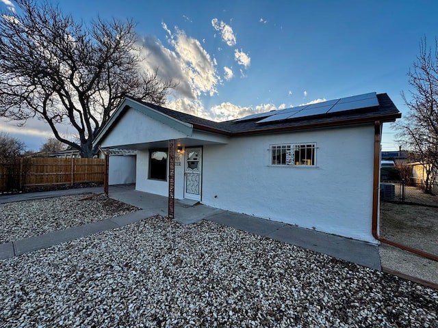 ranch-style home featuring solar panels, roof with shingles, fence, and stucco siding