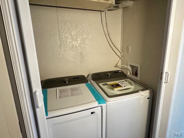 clothes washing area featuring a textured wall, laundry area, and independent washer and dryer