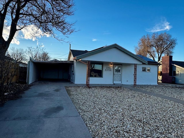 ranch-style home with a carport, concrete driveway, fence, and stucco siding