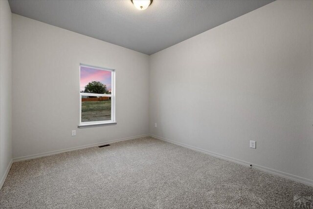 empty room featuring carpet, visible vents, a textured ceiling, and baseboards