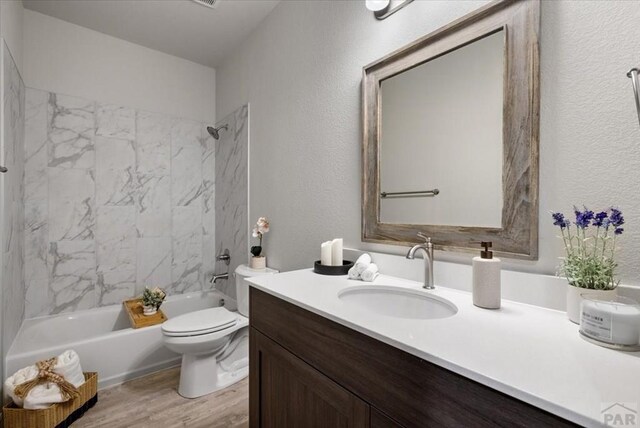 full bath with shower / bath combination, a textured wall, toilet, wood finished floors, and vanity