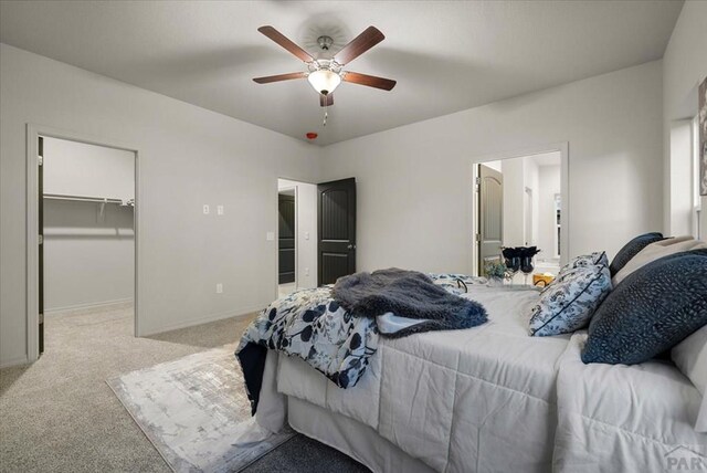 bedroom with light carpet, baseboards, a ceiling fan, a walk in closet, and a closet