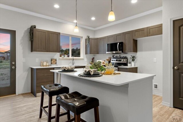 kitchen featuring a kitchen island, light countertops, appliances with stainless steel finishes, decorative light fixtures, and crown molding