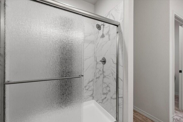 full bath featuring a marble finish shower, baseboards, and wood finished floors