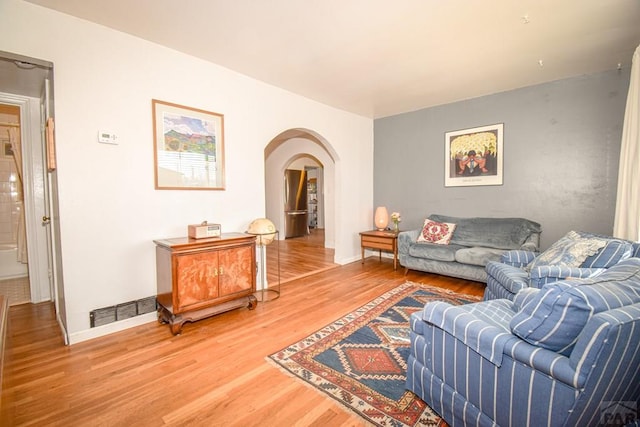 living area featuring light wood-style floors, visible vents, arched walkways, and baseboards