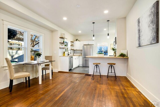 kitchen with a breakfast bar area, open shelves, stainless steel appliances, white cabinets, and a peninsula