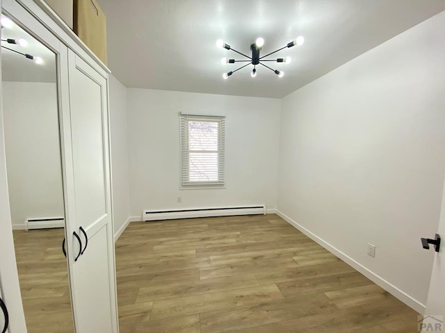 spare room with a baseboard heating unit, a notable chandelier, and light wood-style flooring