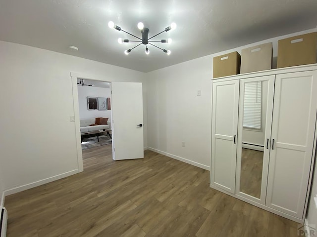 unfurnished bedroom with a baseboard heating unit, wood finished floors, and baseboards