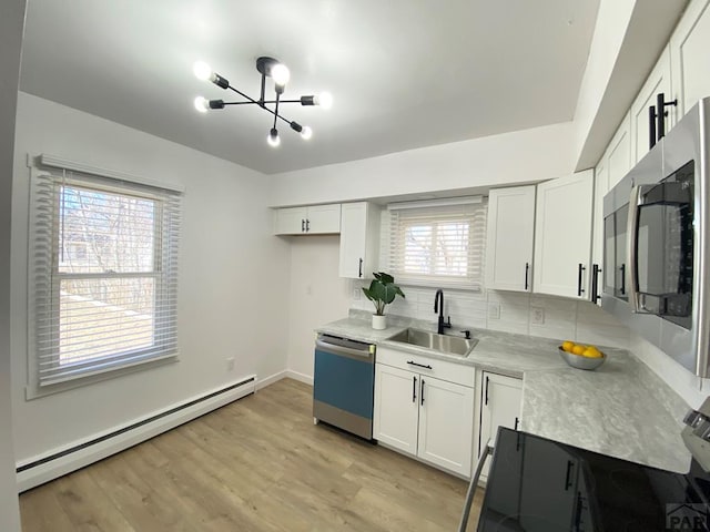 kitchen featuring light wood finished floors, stainless steel appliances, light countertops, a baseboard heating unit, and a sink