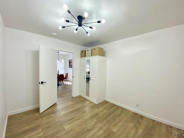 unfurnished room with light wood-type flooring, an inviting chandelier, and baseboards