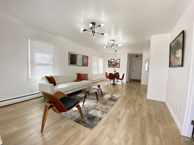 living area with a baseboard radiator, light wood-style flooring, baseboards, and an inviting chandelier