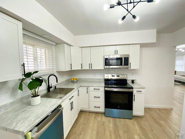 kitchen featuring light wood-style flooring, a sink, light countertops, appliances with stainless steel finishes, and backsplash