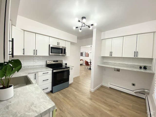 kitchen with light wood finished floors, white cabinets, appliances with stainless steel finishes, light countertops, and a chandelier