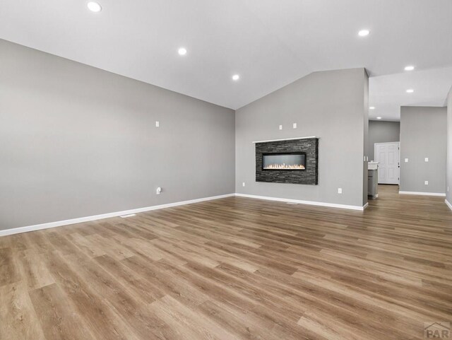 unfurnished living room with recessed lighting, a fireplace, baseboards, vaulted ceiling, and light wood-type flooring