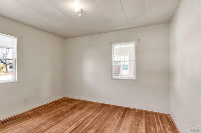 empty room featuring wood finished floors, visible vents, and baseboards