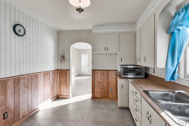 kitchen with a wainscoted wall, arched walkways, white cabinets, and a sink