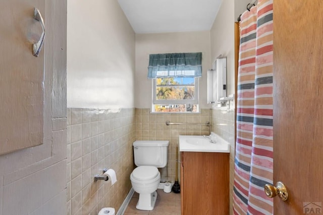 bathroom featuring a wainscoted wall, tile walls, toilet, vanity, and tile patterned floors