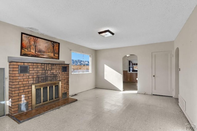 unfurnished living room featuring arched walkways, a textured ceiling, a fireplace, and visible vents