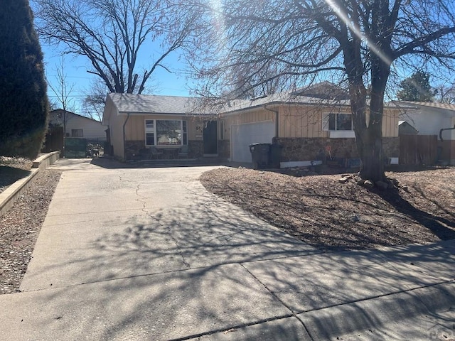 ranch-style home featuring concrete driveway, an attached garage, fence, and stone siding