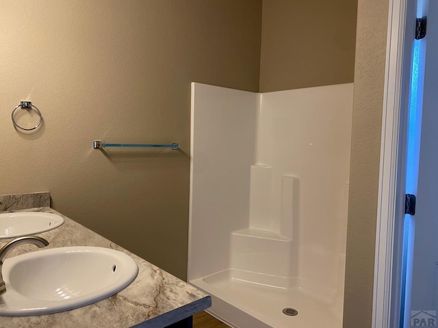 bathroom with double vanity, a walk in shower, and a sink