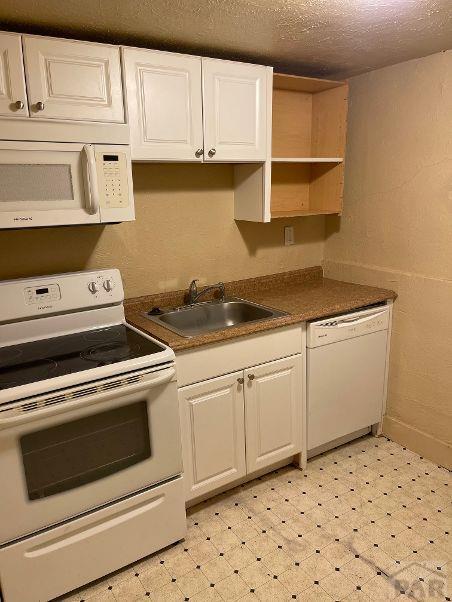 kitchen with light floors, dark countertops, white cabinetry, a sink, and white appliances