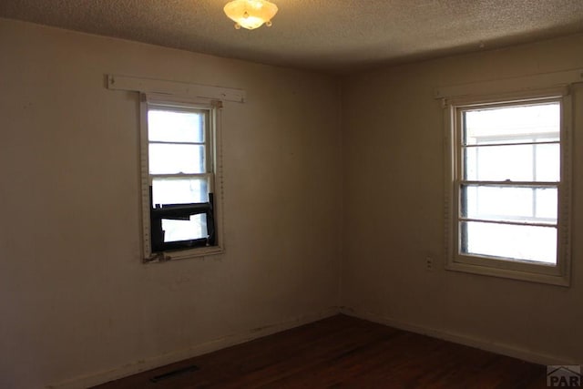 empty room with a textured ceiling, dark wood-type flooring, plenty of natural light, and baseboards