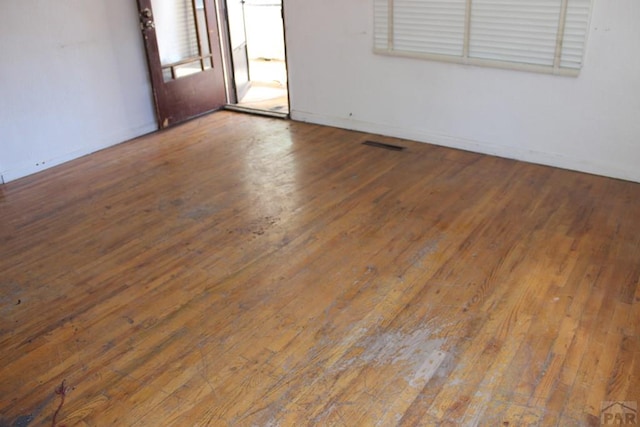 unfurnished room featuring baseboards, visible vents, and wood finished floors