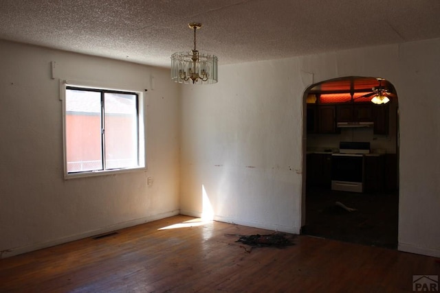 spare room with a textured ceiling, arched walkways, a chandelier, wood finished floors, and visible vents