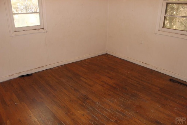 unfurnished room featuring a wealth of natural light, visible vents, and dark wood-type flooring