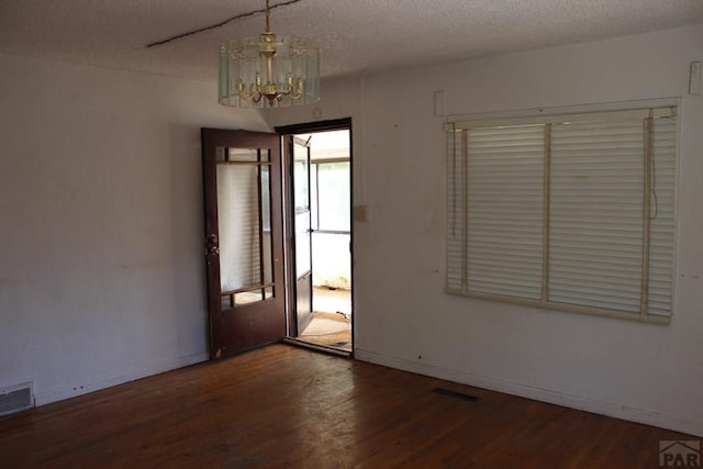 spare room featuring a textured ceiling, wood finished floors, visible vents, and an inviting chandelier