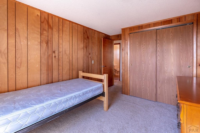 carpeted bedroom featuring wood walls, a textured ceiling, and a closet