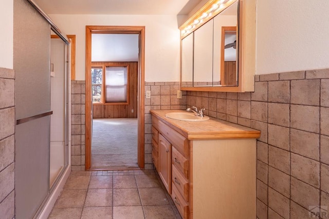 full bath featuring a stall shower, vanity, tile walls, and a wainscoted wall